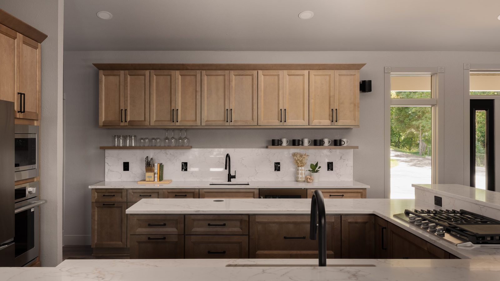 Custom kitchen featuring two-tone maple cabinetry, a marble slab backsplash, quartz countertops, and matte black fixtures.